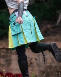 The kilt is knee-length, featuring a clean, flat front panel with a traditional pleated design along the sides. Two large cargo pockets are positioned on each side, with secure flaps and button closures. The waistband includes belt loops and adjustable straps for a customizable fit, and the fabric is a durable, sturdy material suited for rugged use.
