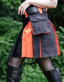 A side view of the Black & Emberglow Hybrid Kilt, displaying the combination of smooth black fabric and emberglow orange pleats, with the metal buckles and utility pockets adding a contemporary, practical touch to the classic kilt design.